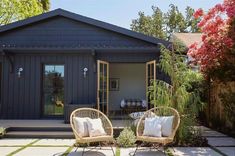 two wicker chairs sitting on top of a stone patio next to a small house