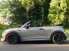 a grey mini convertible parked on the side of the road with trees in the background