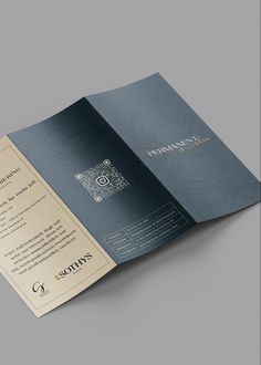 an open brochure is shown on a gray surface with gold lettering and designs