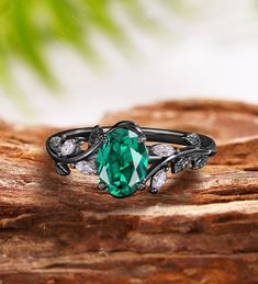 a ring with a green stone surrounded by white diamonds on top of a piece of wood