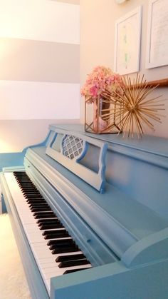 a blue piano in a room with striped walls and flowers on the shelf above it