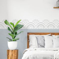 a bed with white sheets and pillows next to a potted plant on a wooden stand