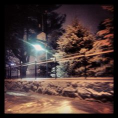 a tennis court covered in snow next to a fence and street light at night time