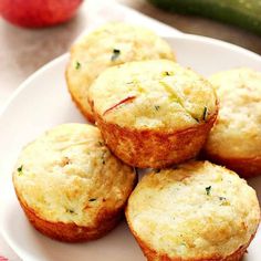 several small muffins on a white plate next to an apple and cucumber