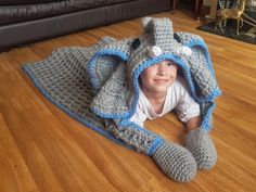 a little boy is laying on the floor in a crocheted elephant blanket that he made