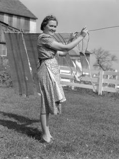 an old black and white photo of a woman hanging out her clothes on a line