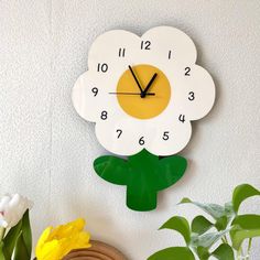 a clock that is on the side of a wall with flowers in front of it