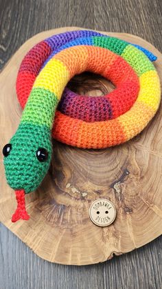 a colorful knitted snake on top of a wooden plate next to a small button