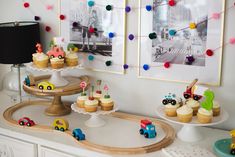 there are cupcakes and cakes on the table in front of two framed pictures