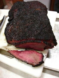 a large piece of meat sitting on top of a cutting board next to a knife and fork