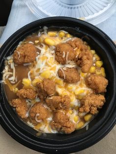 a black bowl filled with corn, meat and cheese covered in gravy on top of a table