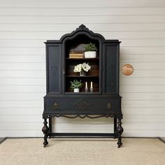 an old fashioned china cabinet with flowers and candles on the top shelf, in front of a white wall