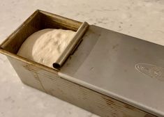 a loaf of bread in a metal box on a marble counter top, with the lid partially open