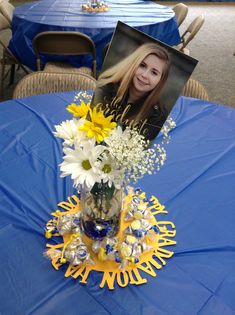 a blue table topped with a vase filled with white and yellow flowers next to a photo