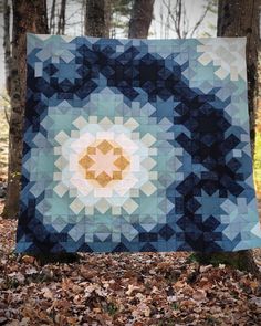 a blue and yellow quilt is hanging on a tree in the woods with leaves around it