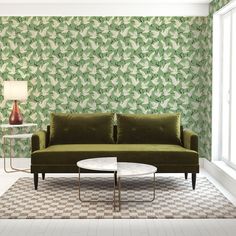 a green couch sitting in front of a white table next to a wall with leaves on it