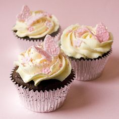 three cupcakes with white frosting and pink decorations