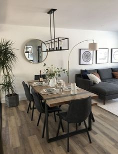 a dining room table and chairs in front of a couch with pictures on the wall