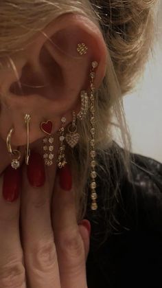 a close up of a person's ear with some piercings on it and a red manicure