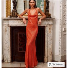 a woman standing in front of a fire place wearing an orange evening dress with sequins