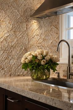 a vase with white flowers sitting on top of a kitchen counter next to a sink