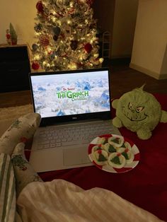 a laptop computer sitting on top of a bed next to a plate of cookies and a christmas tree