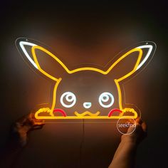 a person holding up a neon sign with a glowing pikachu face on it