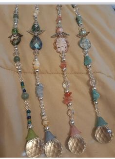 four different necklaces are hanging from a bed sheet with beads and charms on them