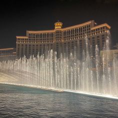 the fountains in front of the hotel and casino are lit up at night with lights on