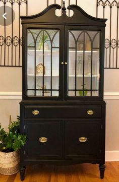 a black china cabinet sitting on top of a wooden floor next to a potted plant