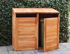 a wooden trash can sitting next to a bush