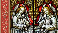 two angels sitting next to each other in front of a stained glass window with writing on it