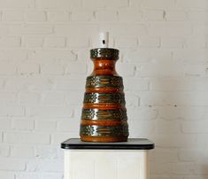 a brown and black vase sitting on top of a white table next to a brick wall