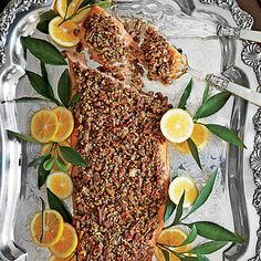 a fish covered in nuts and oranges on a silver platter with spoons