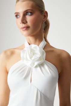 a woman wearing a white dress with a flower on the neck