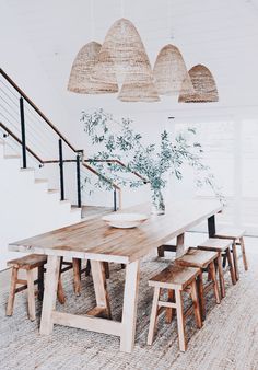 a dining table with four stools under some hanging lights in a white walled room