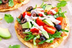 an open pita topped with lettuce, tomatoes, black olives and avocado