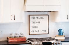 a kitchen with white cabinets and a sign on the stove top that says do small things with great love