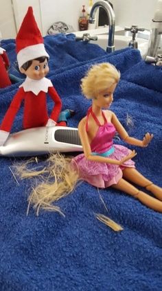 two elf dolls sitting on top of a blue towel next to a hair dryer