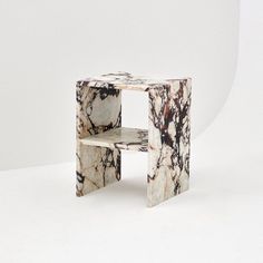 a white and black marbled side table sitting on top of a white floor next to a wall