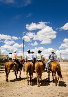 four people are riding horses in an open area with blue sky and clouds behind them