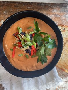 a black bowl filled with soup and vegetables on top of a white cloth next to a wooden table