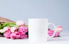 a white coffee mug sitting next to pink tulips