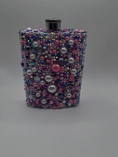 a flask covered in lots of different colored beads and pearls on a gray background