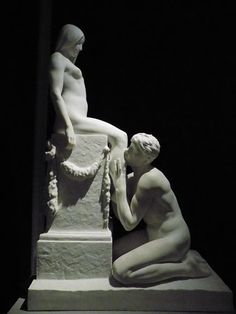 two statues sitting next to each other in a dark room and one is touching the arm of another statue