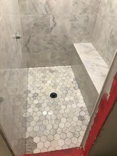 a shower stall with red and white tile on the floor, walls and floors that are covered in marble hexagon tiles