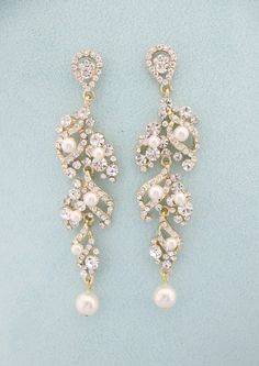 two pairs of pearl and crystal earrings on a blue surface with white pearls in the middle