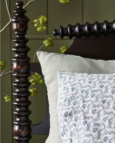 a close up of a pillow on a bed near a wooden headboard with green leaves