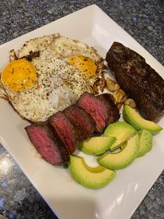 steak, eggs, and sliced avocado on a white plate with granite counter top