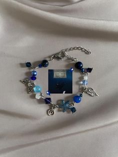 a bracelet with blue beads and angel charms on it is laying on a white cloth